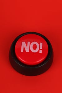 Close-up of a red button with "NO" text, set on a vivid red background. Ideal for concepts of denial or negativity.